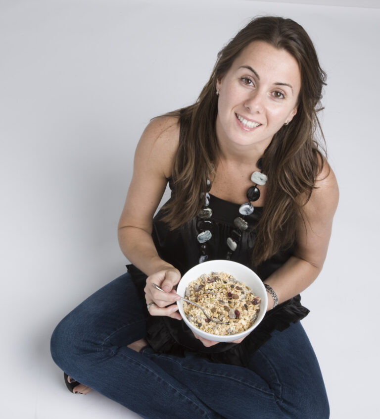 A woman sitting on the floor holding a bowl of cereal.