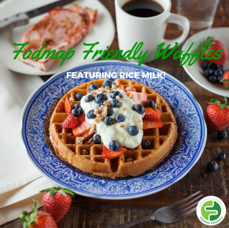 A plate with a waffle topped with whipped cream, strawberries, blueberries, and granola. A cup of coffee, strawberries, and a plate with toast are in the background. Text reads Fodmap Friendly Waffles featuring rice milk.