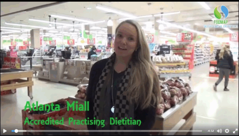 A woman with long blonde hair stands in a supermarket produce section, speaking to the camera. Green text on the screen reads, Atlanta Miall, Accredited Practising Dietitian. FODMAP logo is in the top right corner.