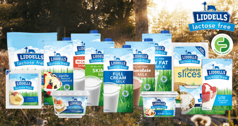 An assortment of Liddells lactose-free dairy products, including milk, cheese, custard, sour cream, and cheese slices, displayed outdoors with a Liddells logo and a green health tick symbol in the top right corner.