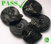 Five round pieces of black liquorice sweet are shown. The word PASS and a green tick appear in the top left corner, with a green circular logo in the bottom right corner.