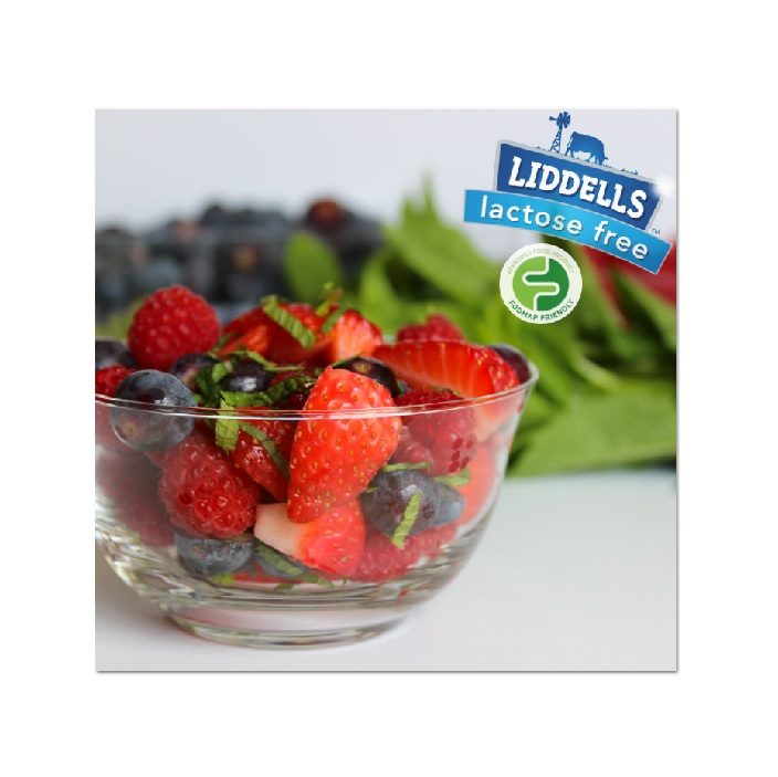 A glass bowl filled with fresh strawberries, blueberries, and raspberries sits in front of leafy greens. The image has a Liddells lactose free label in the top right corner.