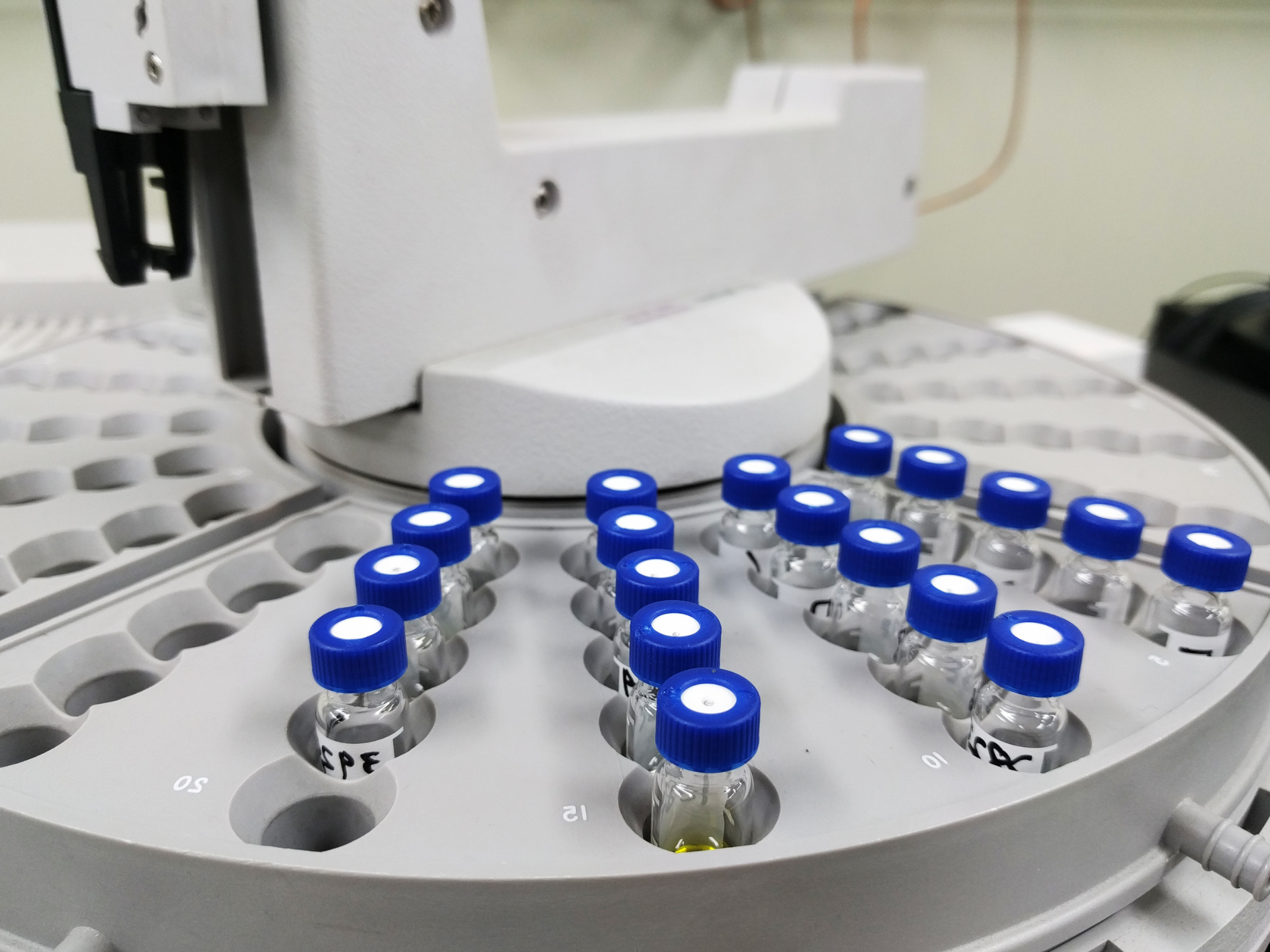 Close-up of a laboratory autosampler tray holding multiple glass vials with blue caps, arranged in a circular pattern, ensuring lab-tested accuracy for automated chemical analysis.
