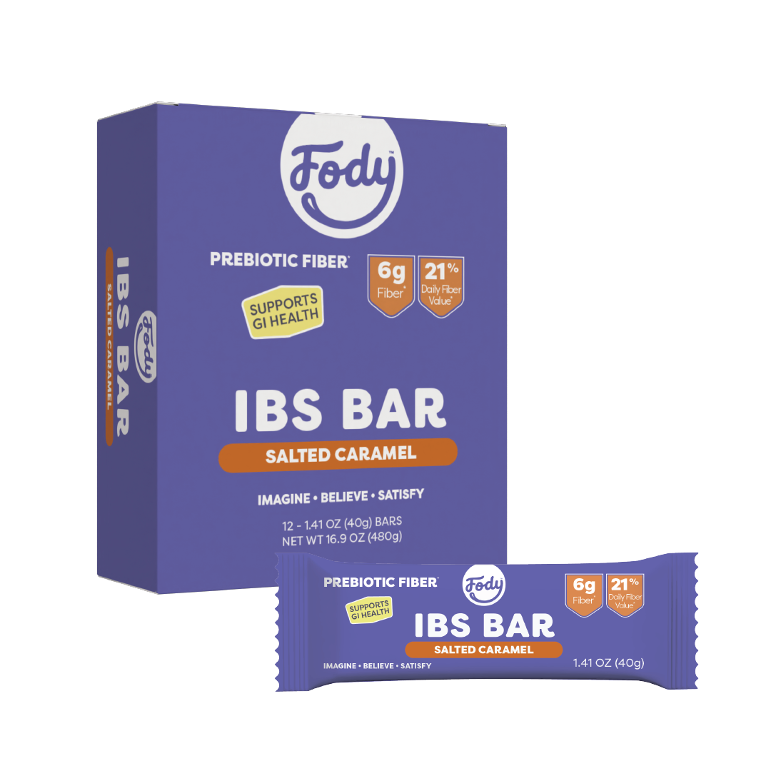 A box and a single wrapped Fody Salted Caramel Snack Bar. The purple packaging with orange and white text highlights its high fibre content, featuring “prebiotic fibre,” “6g fibre,” and “21% daily fibre value.”.