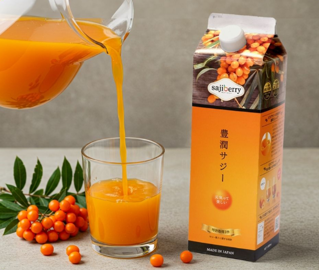 A carton of Finess' Hojun Saji sea buckthorn juice labelled sajiberry stands next to a glass being filled with orange juice from a jug. Orange sea buckthorn berries and green leaves, perfect for a FODMAP Friendly diet, are arranged nearby.
