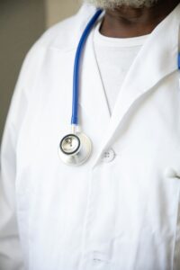 A person wearing a white lab coat and a stethoscope around their neck, suggesting they are a healthcare professional who may help explain symptoms or causes of health conditions. Their face is not visible in the image.