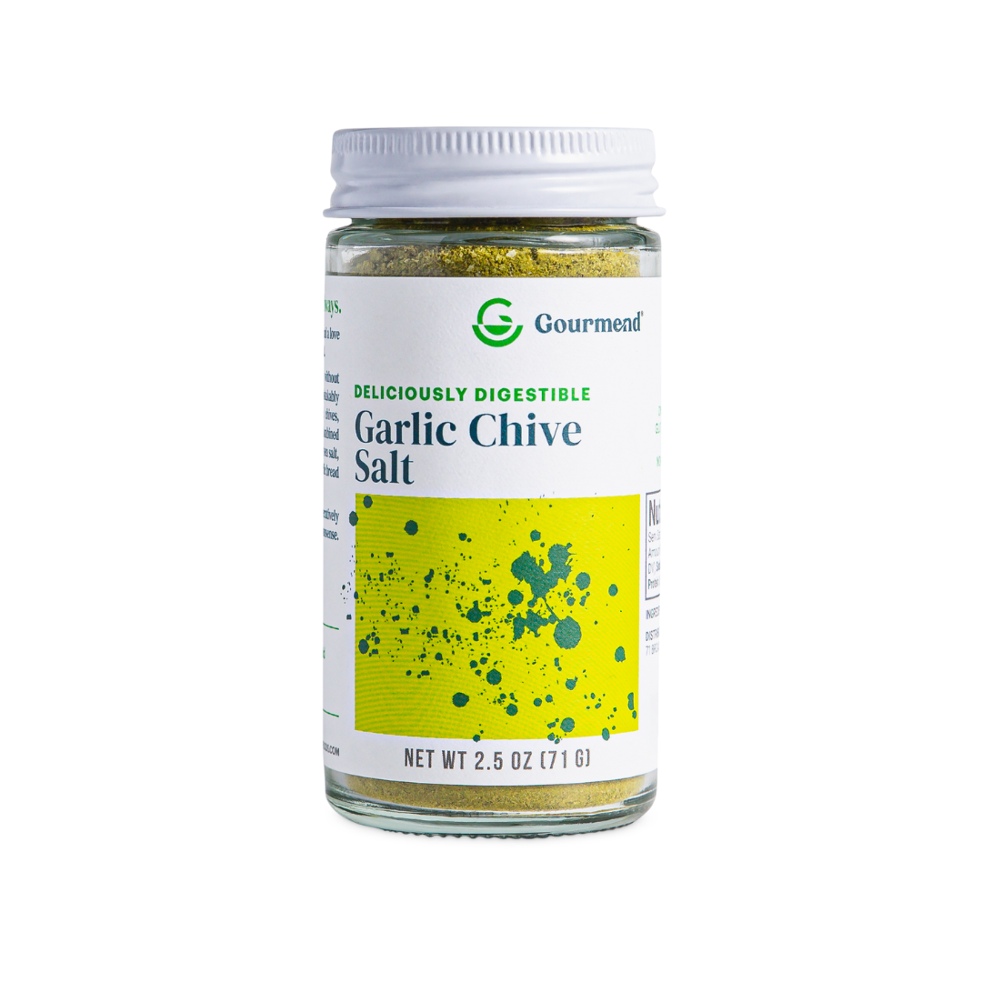 A glass jar of Gourmend Garlic Chive Salt with a green and yellow label, featuring the text Deliciously Digestible and Net Wt 2.5 oz (71 g) on the front. Perfect for elevating any dish with flavourful garlic salt.