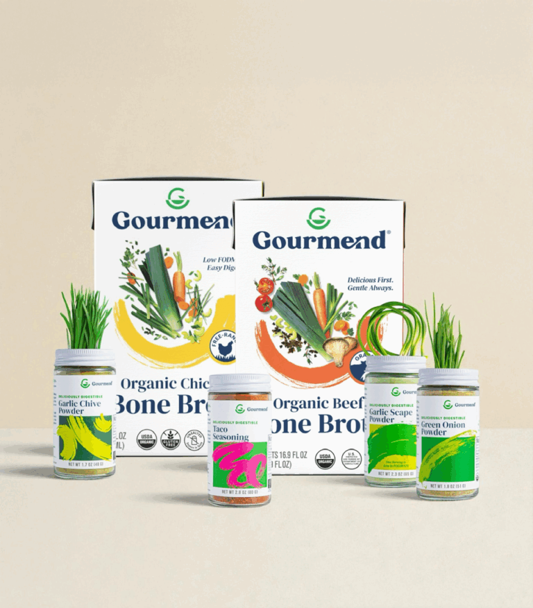 A display of Gourmend products features FODMAP Friendly organic chicken and beef bone broths, plus four jars of seasonings—garlic chive, taco, spring onion, and garlic scape—alongside fresh chives and onions in jars.