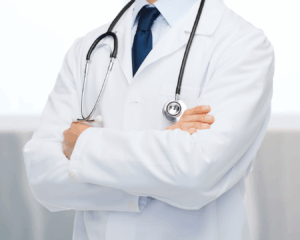 A doctor in a white lab coat with a stethoscope around their neck stands with arms folded. The head is not visible, and the doctor wears a blue shirt and tie, representing trusted Gut Health Experts with Low FODMAP Certification.